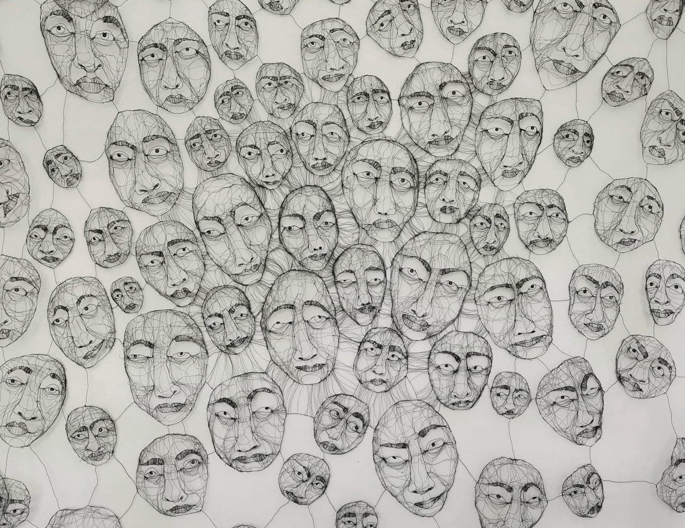 A wall of Fiona Morley's wire faces, dozens of them strung together by fine threads of wire, each with its own expression